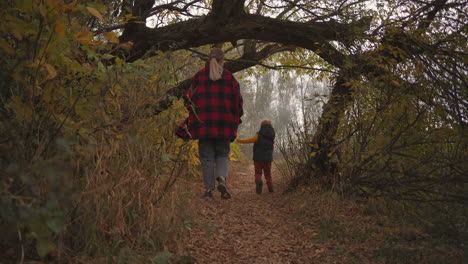 family of mother and little son are having fun in forest at autumn day running over path following shot happiness and joy of woman and boy at weekend