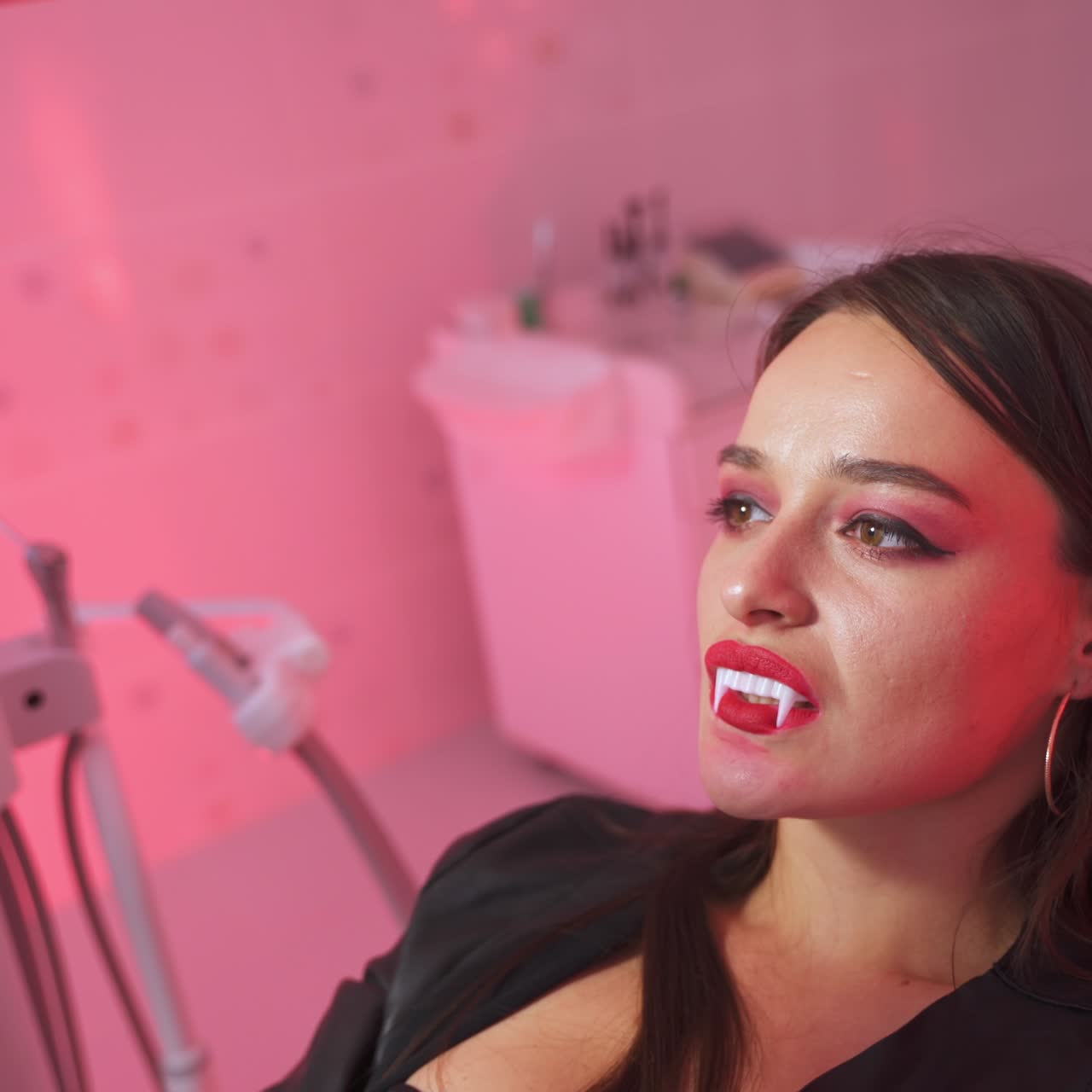 Vampire lady sitting at dentist's chair and holding a mirror in front of her. Woman is happy about her beautiful white monster teeth