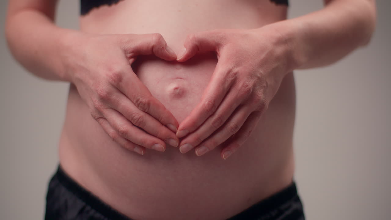 Donna che posa le mani a forma di cuore sulla pancia incinta