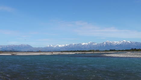 river flows steadily before snow-topped foothills on a clear summer's day - waimakariri river