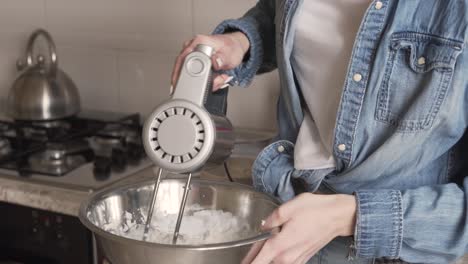 a beautiful girl blends the flour, butter and other ingredients in a large silver bowl in order to make cream for a cake