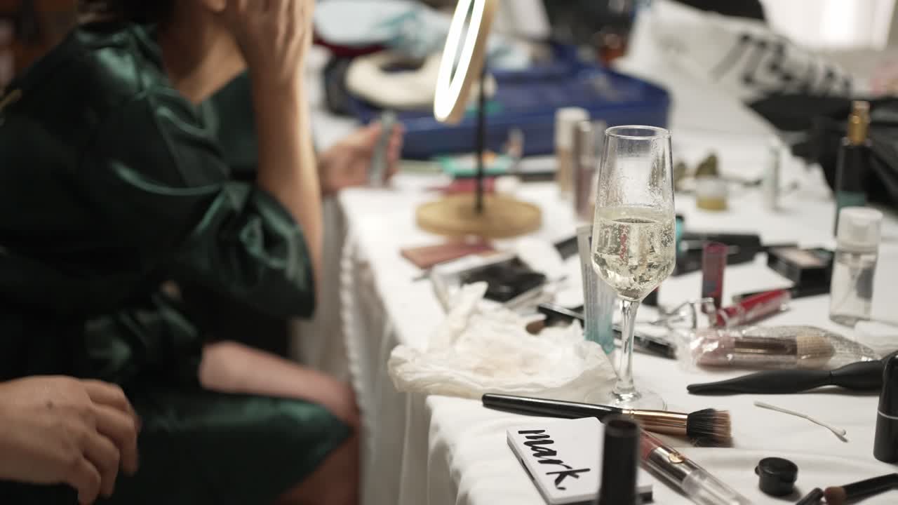 Person preparing makeup at a table with cosmetics and a glass of champagne, creating a festive mood