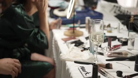 person preparing makeup at a table with cosmetics and a glass of champagne, creating a festive mood