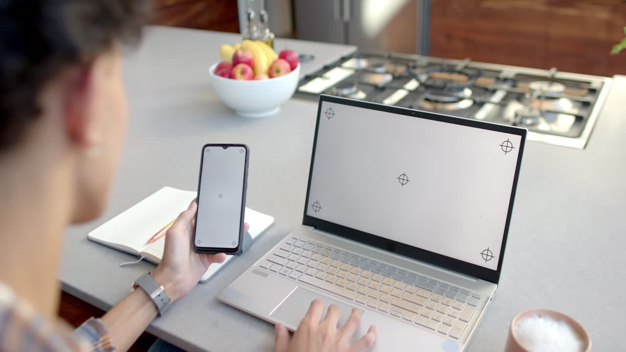 Using smartphone and laptop, teenage boy working from home at kitchen counter, copy space