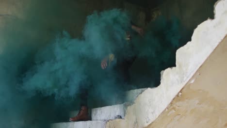 mixed race man holding green flare sitting on stairs in an empty building