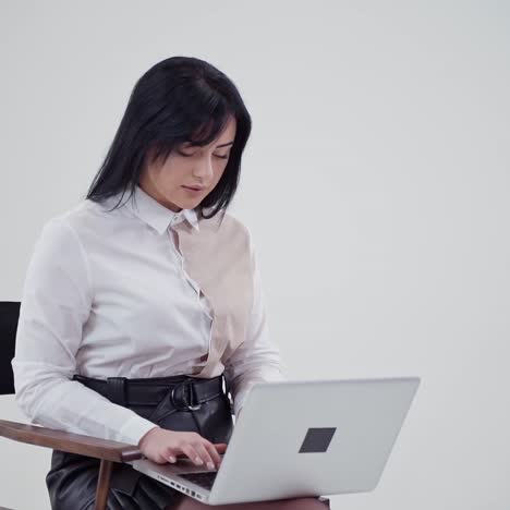 beautiful woman is typing on a laptop. attractive girl in white blouse sitting on the chair and printing on a modern gadget. slow motion.