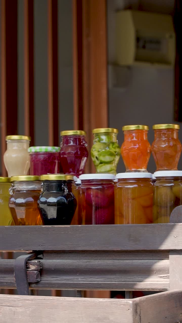 Vibrant jars filled with a variety of homemade preserves are artistically arranged at a quaint market stall, basking in the warm sunlight and inviting passersby to stop and admire