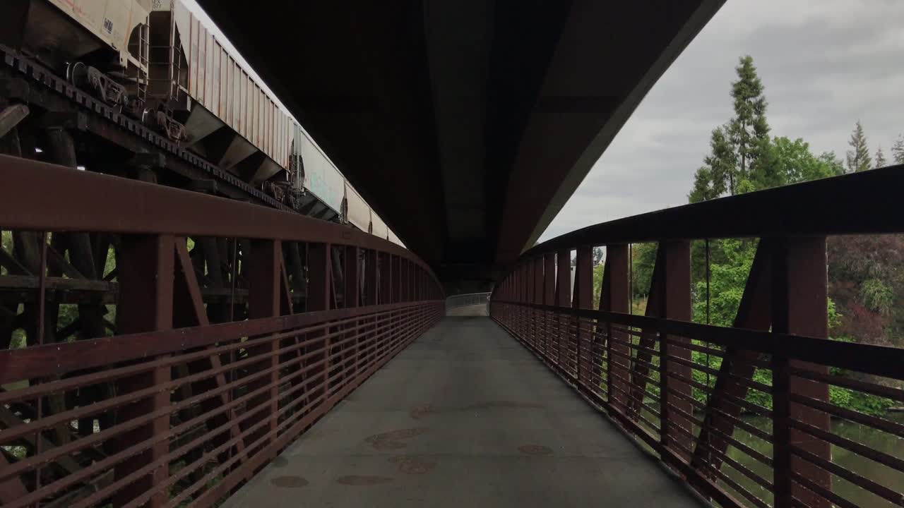 백그라운드에서 운전하는 표시되지 않은 화물 열차가 있는 강 위의 금속 인도교의 핸드헬드 샷