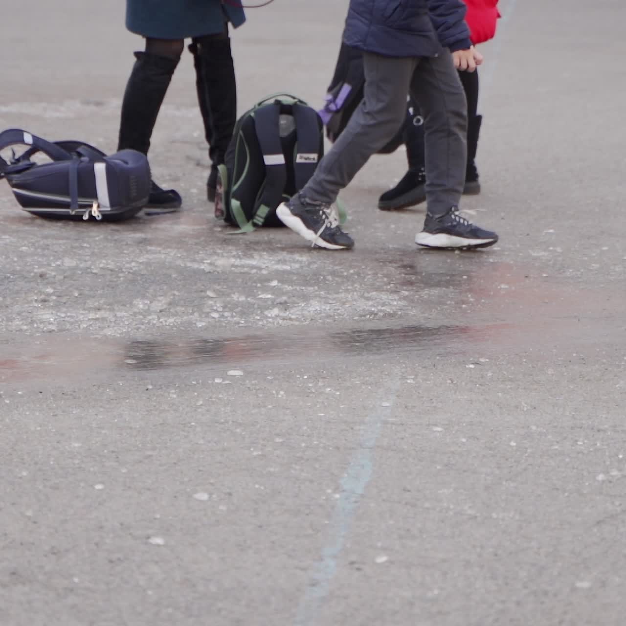 Close-up of children's feet. Happy school kids slide on the ice in the schoolyard. Frosty winter day.