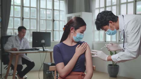 medical doctor in safety gloves and protective mask is making a vaccine injection to a female patient in a health clinic. doctor uses hypodermic needle and a syringe to put a shot of drug as treatment