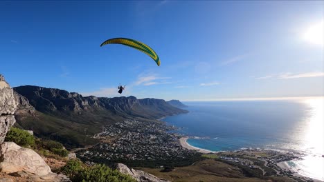 slow motion footage of a paraglider flying towards a big wall of cliffs and blue ocean in the background