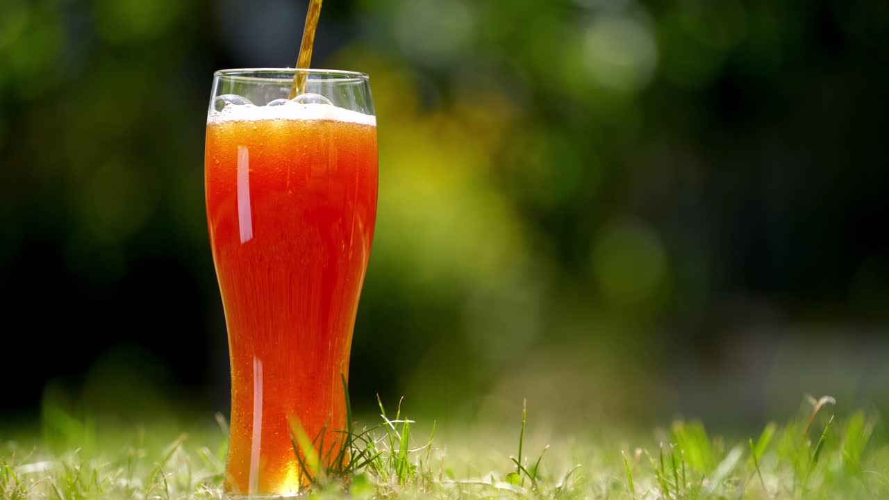 gießen sie frisches bier in das glas im freien. dunkles bier fließt von oben in ein glas-close-up. pint kaltes craft-bier isoliert auf grünem hintergrund.