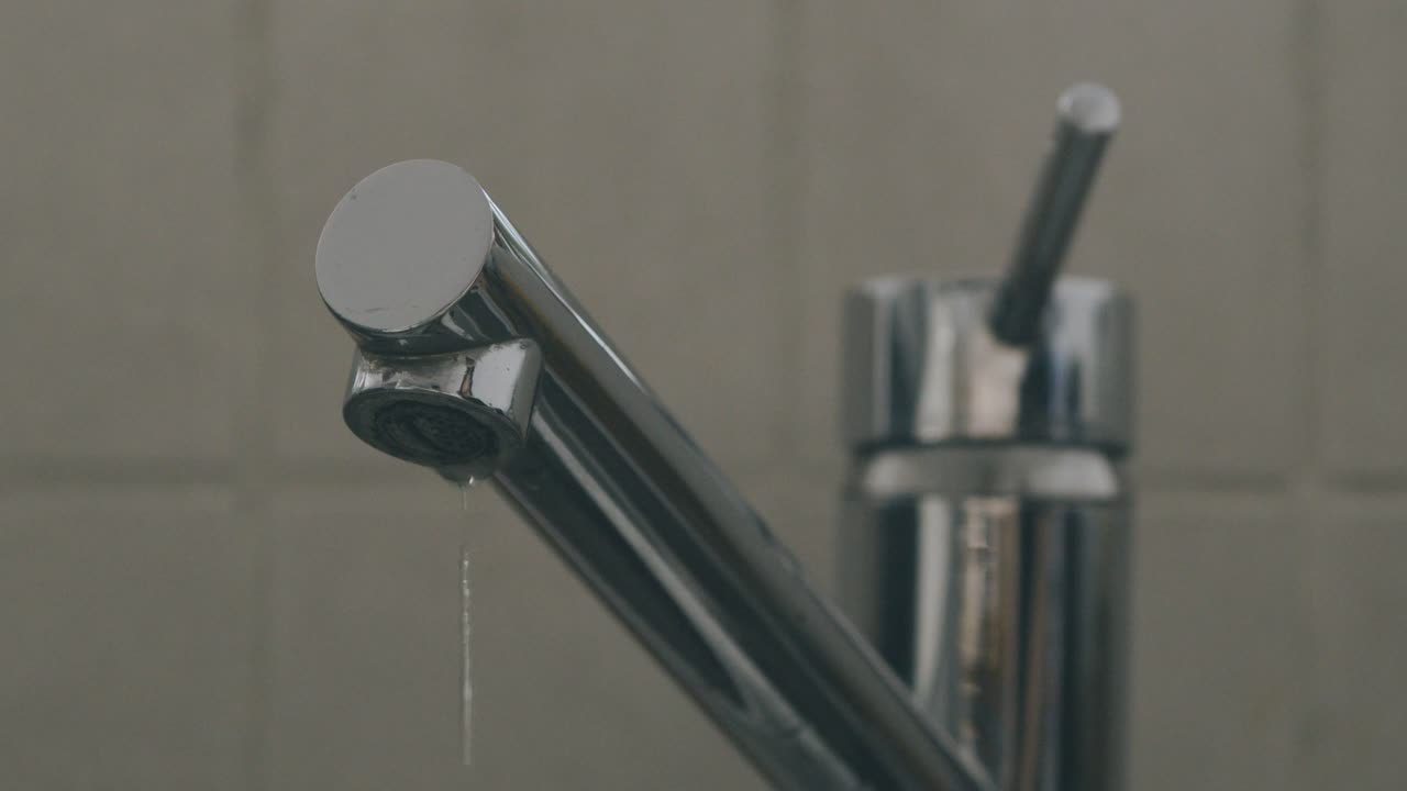 Una goccia d'acqua cade dal rubinetto del lavandino al rallentatore, rubinetto completo.