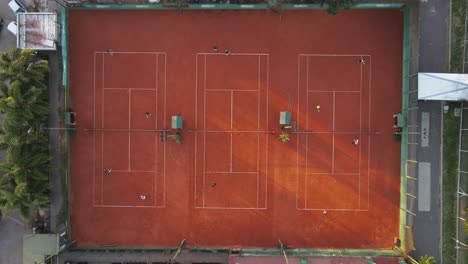 aerial view in slow motion of clay tennis courts, with people playing wearing white clothes