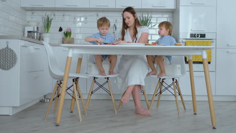 Mom-with-two-children-in-the-kitchen-at-the-table-preparing-burger-for-lunch