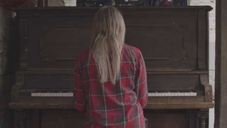 A-young-blonde-haired-woman-in-a-red-flannel-shirt-sits-at-an-old-fashioned-wooden-piano