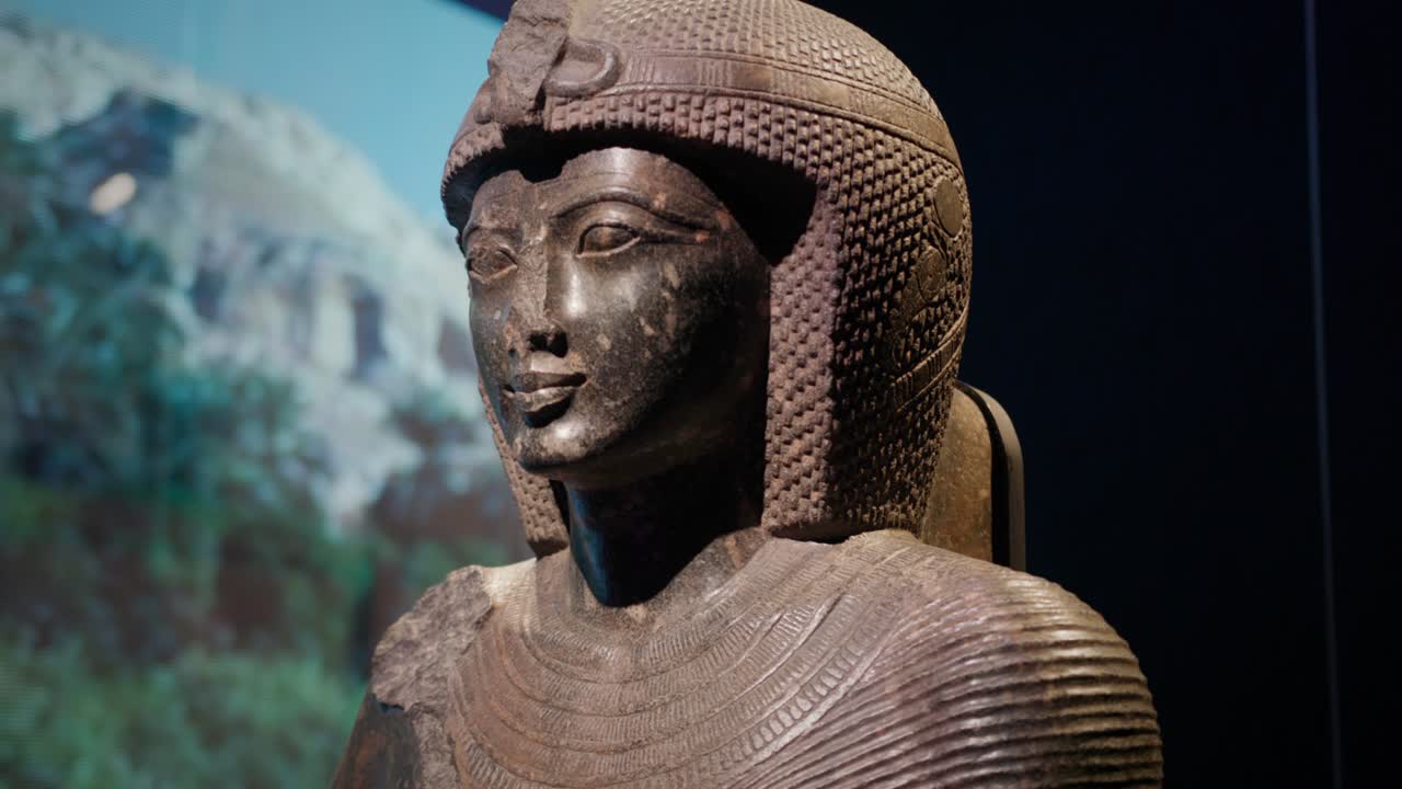 古代エジプトで最も強力なファラオの一人、若き日のラムセス2世を描いた彫像のクローズアップ。この彫刻は、理想化された顔の比率と精巧な頭飾りを特徴としている。