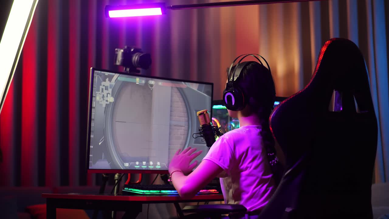 vista trasera de una streamer asiática que se estira mientras juega un juego a través de la red en una computadora personal. videojuego de transmisión en vivo, escritorio iluminado por luz de tira de led rgb
