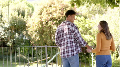 Happy-diverse-couple-standing-on-balcony-and-holding-hands-at-home,-copy-space,-in-slow-motion