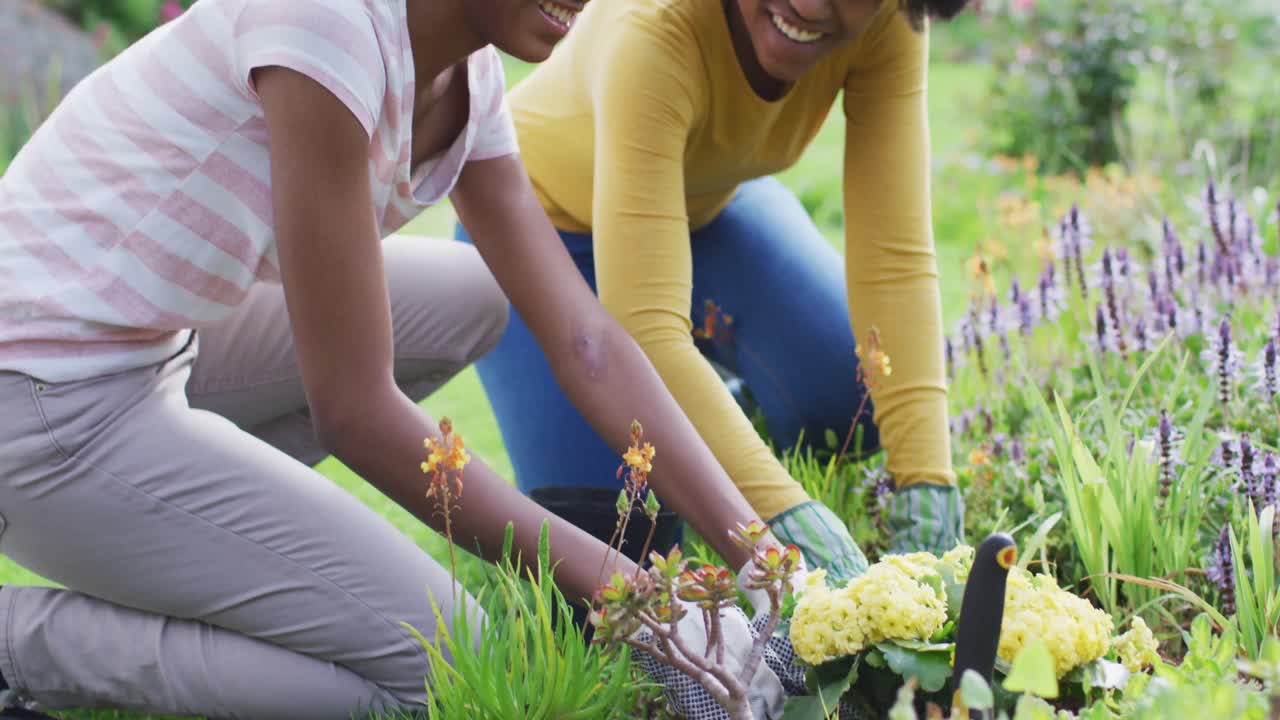 미소 짓는 아프리카계 미국인 어머니 와 딸 이  ⁇ 은 정원 에서 함께 정원 을 꾸리고 있는 초상화