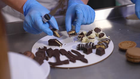 hands in blue latex gloves cut the chocolate sweets on the plate. preparation of desserts for demonstration and degustation. close up.