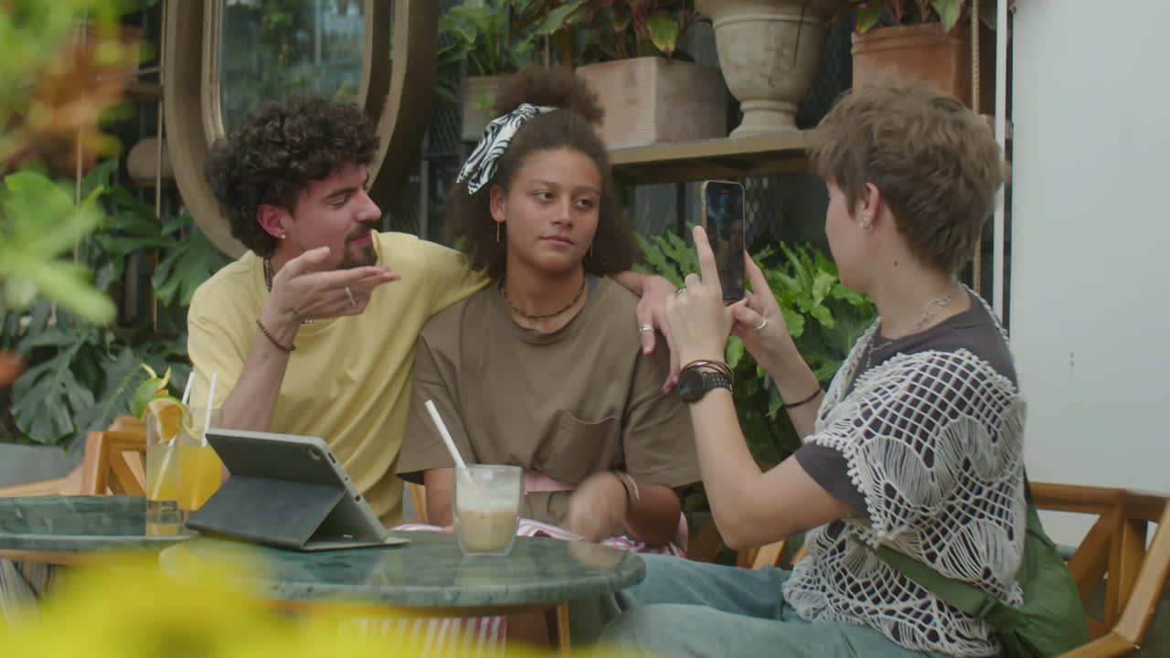 Girl Photographing Friends with Phone in Outdoor Cafe