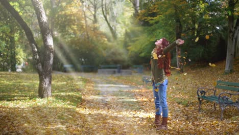 cámara lenta: hermosa joven pelirroja parada en un parque en otoño con hojas cayendo alrededor de ella-1