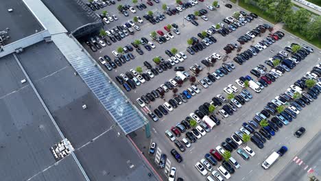 a busy shopping center parking lot with rows of parked cars, aerial view