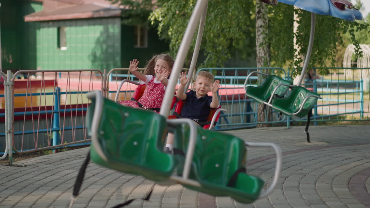 niños pequeños felices agitan las manos montando carrusel en el parque