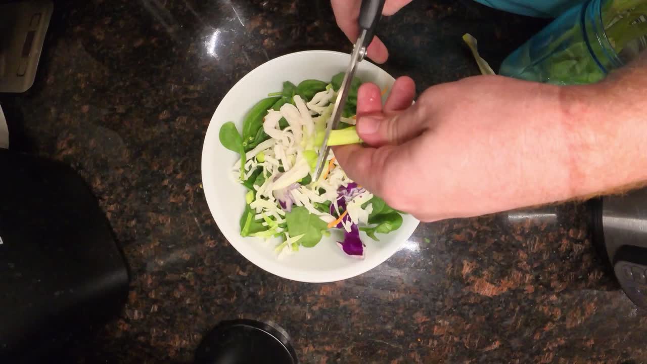 Close up top view footage of a chef expertly cutting spring onion with scissors over a fresh salad for preparing coleslaw