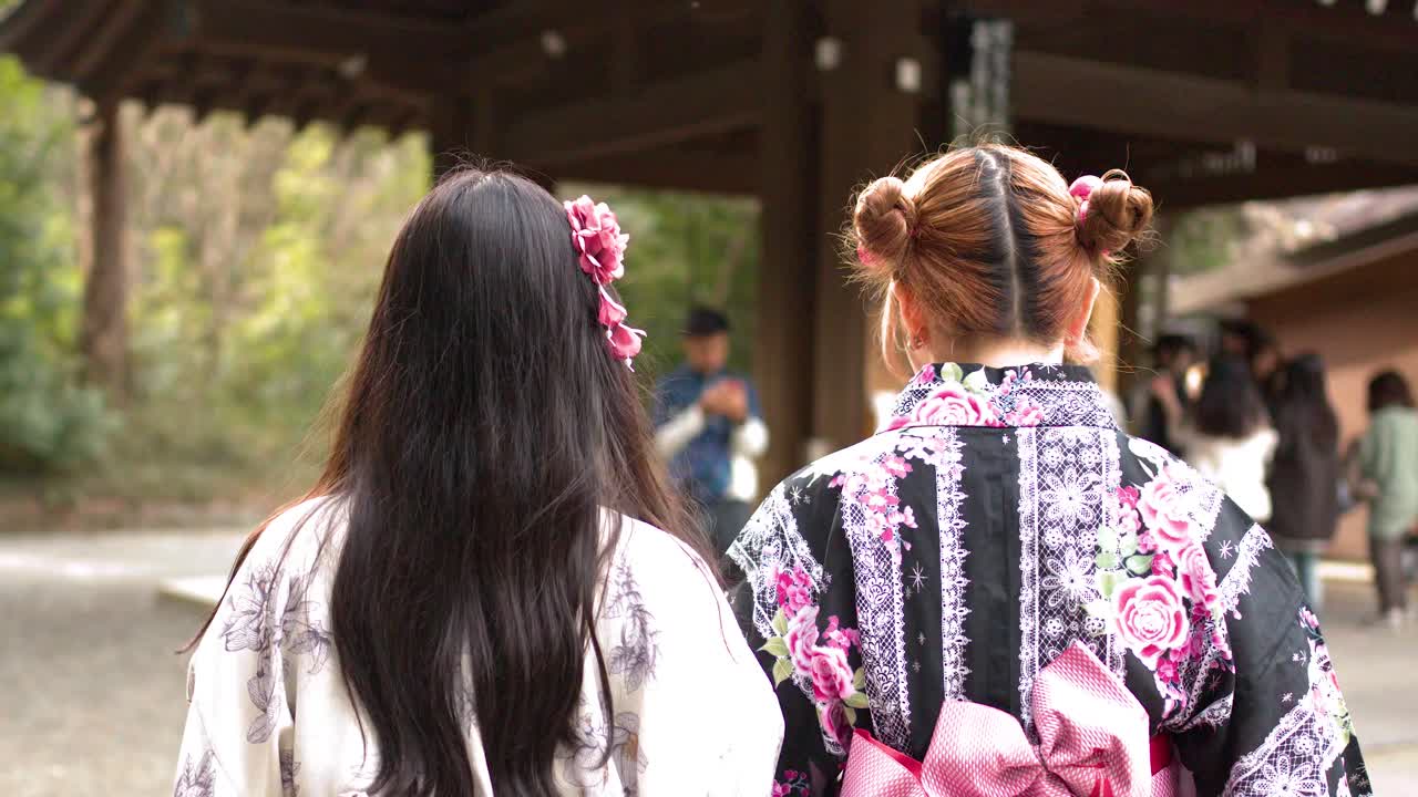 Vista posteriore di due donne che indossano kimono floreali mentre camminano attraverso un santuario storico giapponese.