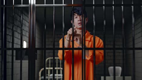 asian male prisoner in handcuffs standing in prison, pointing his finger towards you, speaking against and blaming you