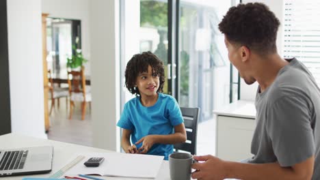 happy biracial man and his son doing homework together, fistbumping