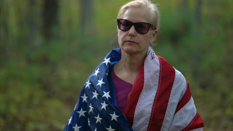 closeup of pretty, blonde woman with an american flag around her and giving the camera the finger