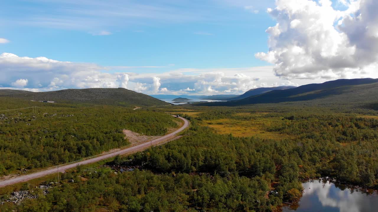 aerial: carretera principal en el norte de suecia entre bosques y lagos con un tráfico muy ligero y con un cielo azul y algunas nubes en el fondo