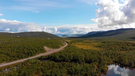 Aerial:-Main-road-in-northern-Sweden-among-forests-and-lakes-with-very-light-traffic-and-with-a-blue-sky-and-some-clouds-in-the-background