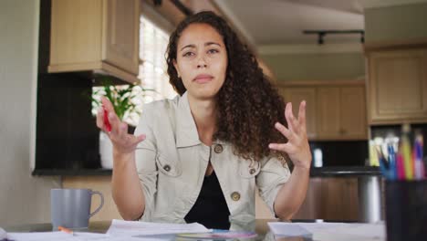 feliz mujer biracial gesticulando en una videollamada en la cocina