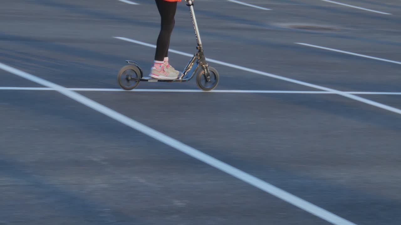 A Girl Rides A Scooter Through An Empty Parking Lot