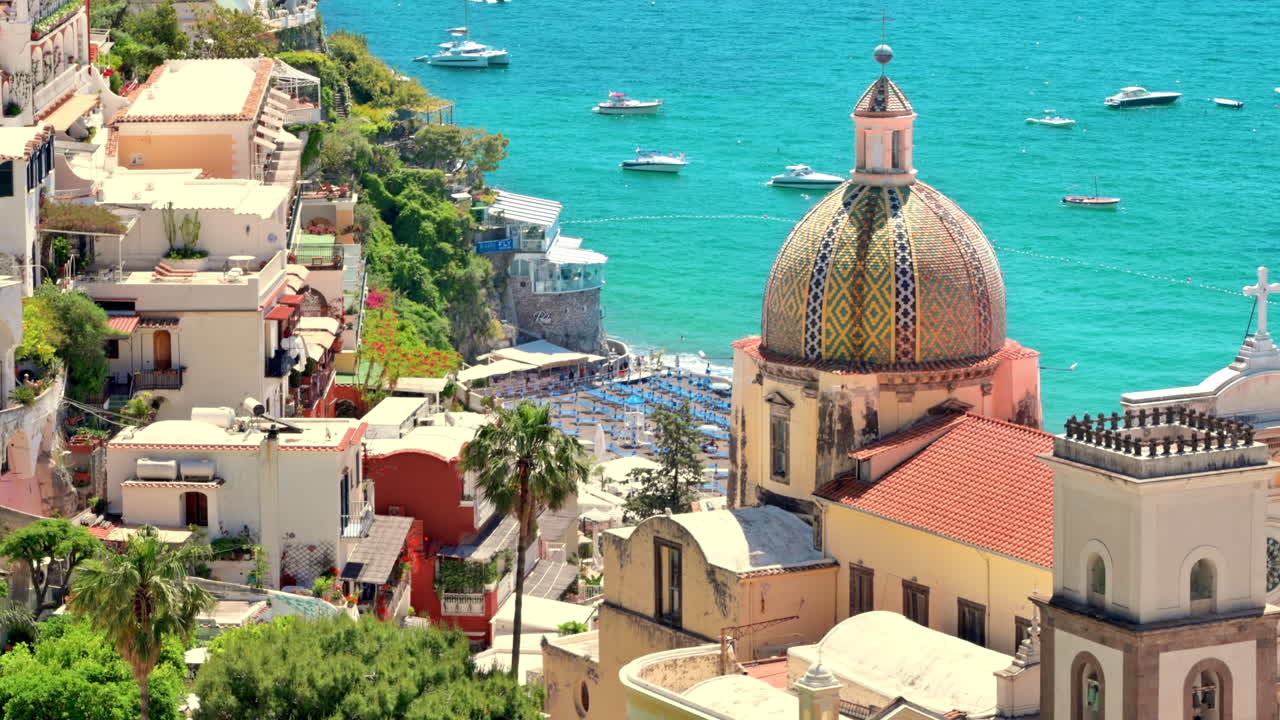 Paesaggio urbano di Positano, situata sulla costa del Mar Tirreno, Italia. File di edifici residenziali, chiesa, vegetazione, spiaggia con persone che si riposano