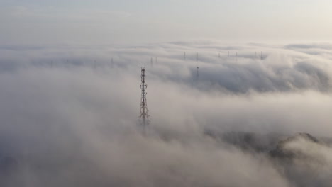 torre de telecomunicaciones en una densa niebla pesada que se mueve sobre las colinas por la tarde