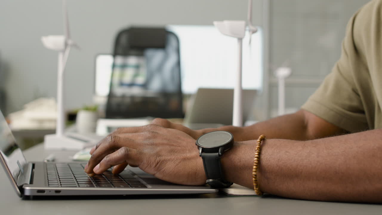 Camera focuses on the hands of african american man typing on keyboard laptop sitting at desk in the office
