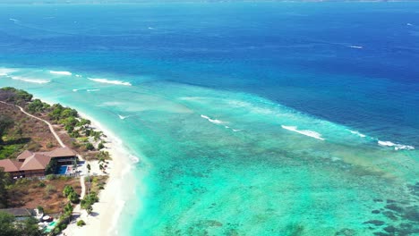 Beach-bar-restaurant-on-tranquil-sandy-shoreline-of-tropical-island-surrounded-by-shallow-turquoise-lagoon-and-deep-blue-sea-with-waves