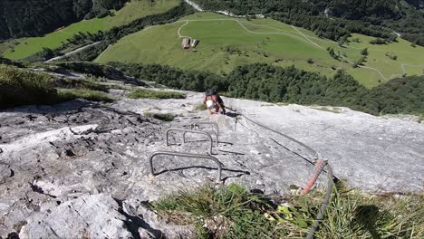 a young man is climbing slow and steady up the side of the mountain, using only the metal pin handles