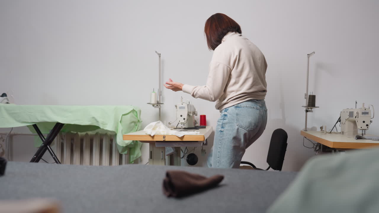 Female costumer walks to sewing machine holding screwing device, then sits before weaving machine, loosening needle part in minimal workshop, focusing on mechanical process and careful precision