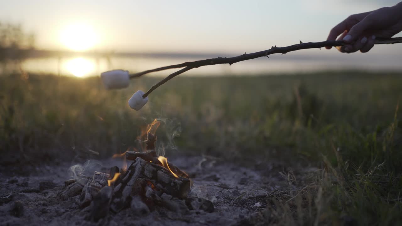 해가 지는 해변에서 불꽃 위에 마쉬멜로를 구워