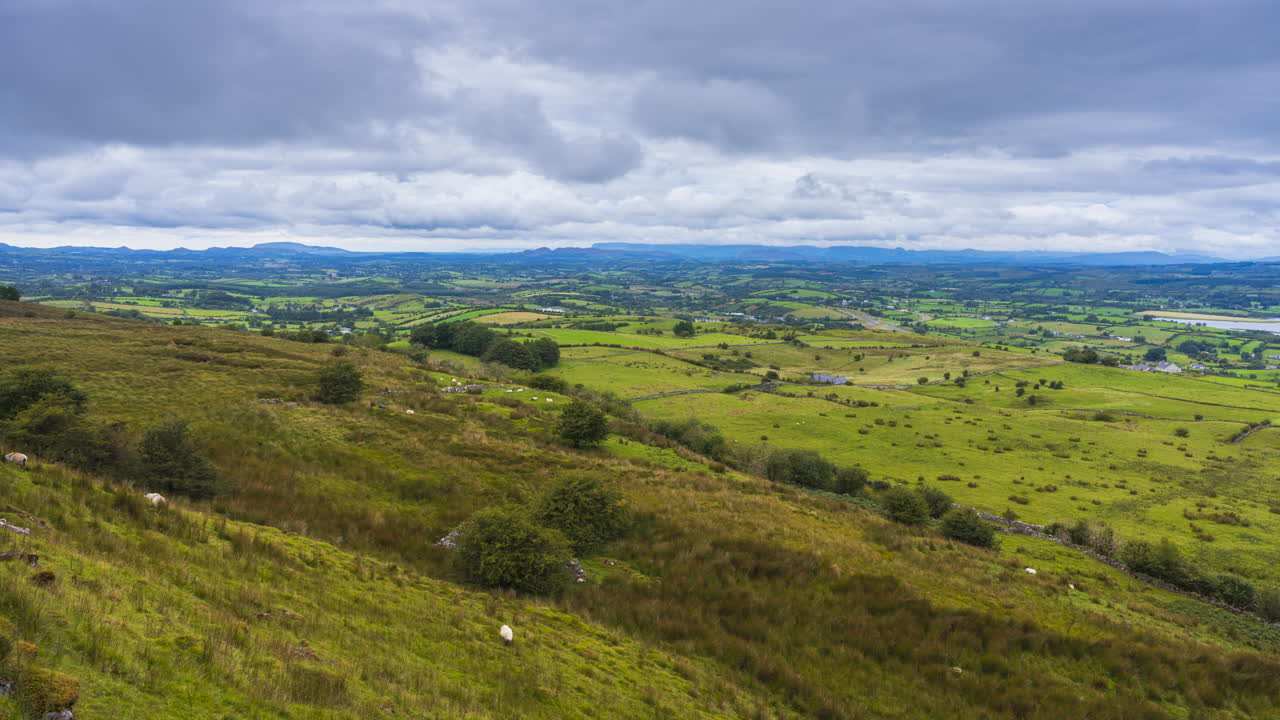 timelapse de la naturaleza rural tierras de cultivo con árboles y ovejas en el campo de primer plano y colinas y casas en la distancia durante un día nublado visto desde carrowkeel en el condado de sligo en irlanda