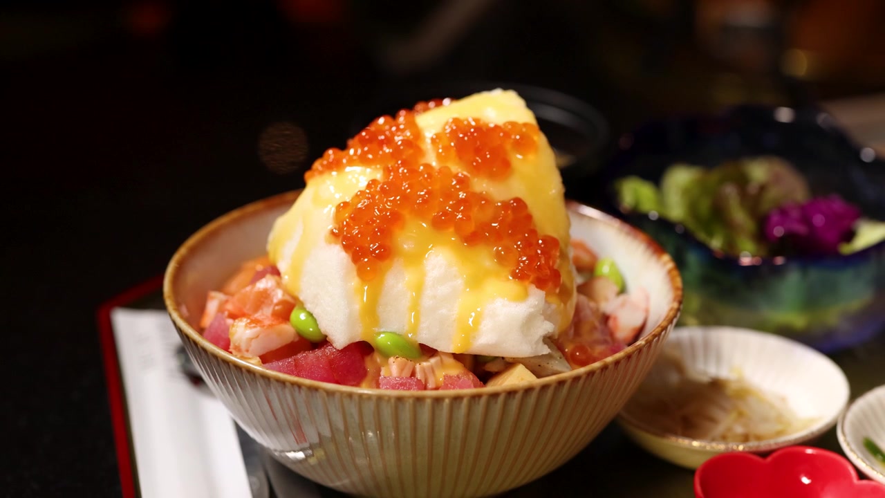 Close-up de ovas de salmão laranja brilhante sendo derramadas sobre uma tigela gourmet de donburi de frutos do mar.