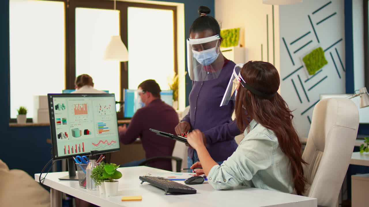 보호 마스크를 착용한 다민족 동료들이 연간 통계를 확인하고 있습니다.