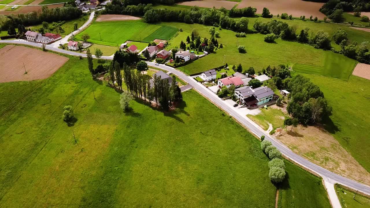 Liukuva ilmakuva Slovenian maaseudusta tietä pitkin, taustalla kukkuloita, taloja ja peltomaita. Pilvinen taivas, Slovenia, Eurooppa.