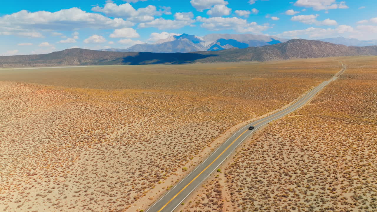 Lonely black car on the road to Nevada, USA. Beautiful sight of desert contrasting with blue skies. Mountains at backdrop.